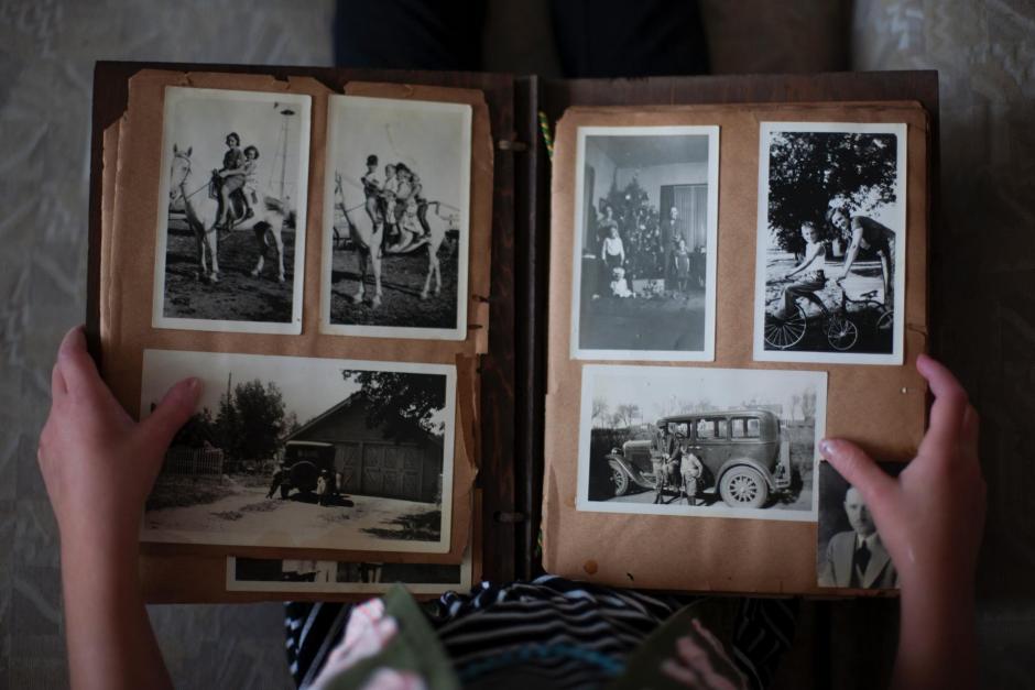 Overhead view of child holding old photo album open in their lap.