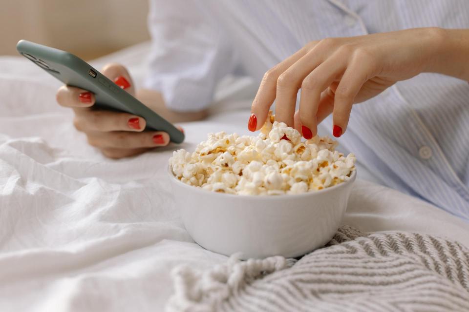/person-with-red-nails-using-a-smartphone-while-eating-popcorn